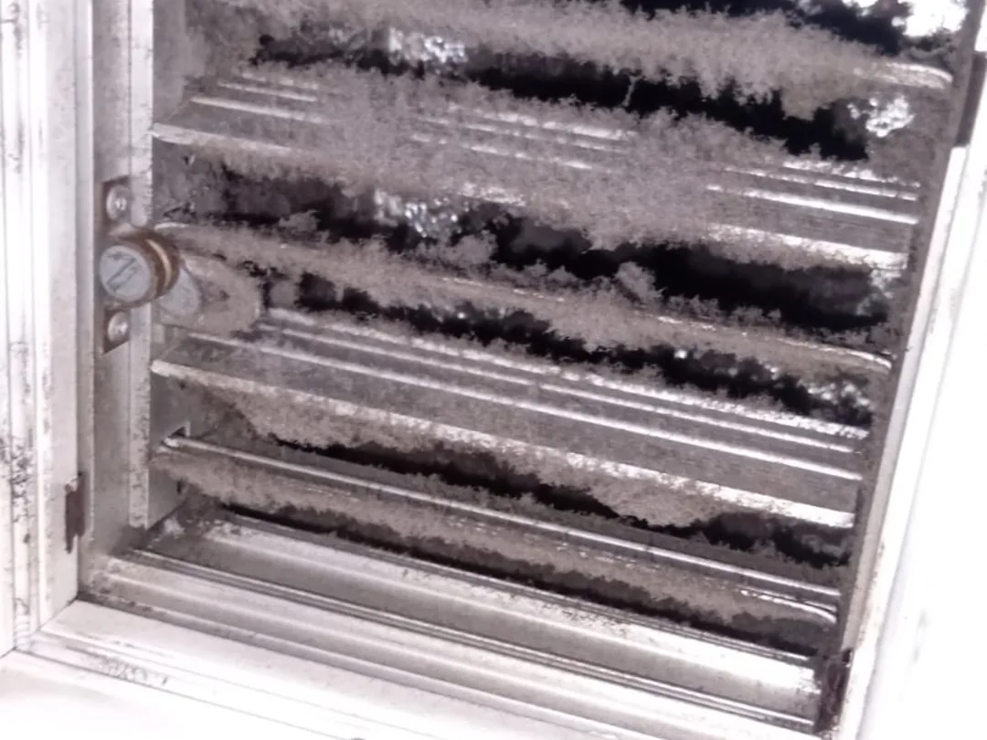 Before cleaning: an evaporator coil whose aluminium fins are choked with a felt of grey dust.