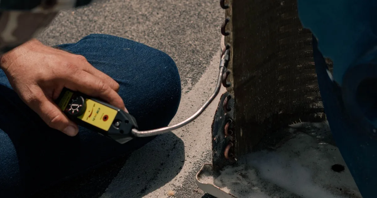 A technician holds a handheld diagnostic tool against the coil of an outdoor air conditioning unit during a service visit.