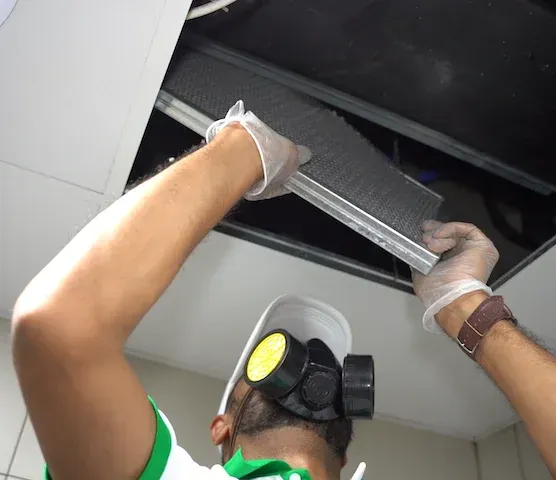 A Homezy technician removing a ceiling AC filter panel to reach the unit behind it.