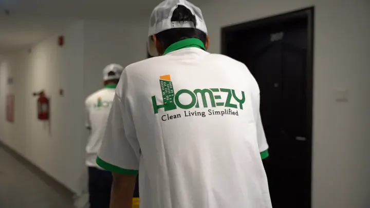 Two Homezy technicians in branded green uniforms arriving at a Dubai apartment with their equipment.
